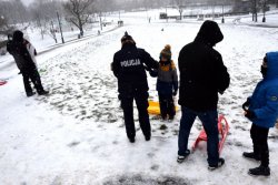 policjantka wręcza dziecku opaskę odblaskową na jednej ośnieżonych górek w parku