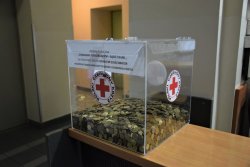 Przezroczysta skrzynia z monetami z logo i napisem Polski Czerwony Krzyż.