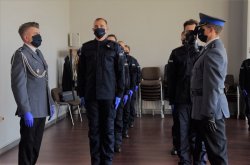 Na pierwszym planie policjant oddający honory Komendantowi KMP w Krakowie, na drugim planie młodzi policjanci stojący w szeregach na baczność.