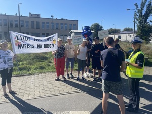 uczestnicy akcji z transparentem z napisem każdy ma swoje miejsce na drodze obok policjantka