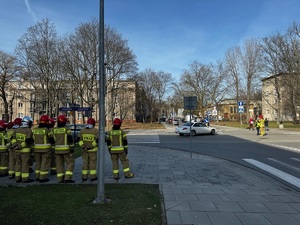 3 grupa strażaków obserwuje kierownie ruchem drogowym przez jednego ze strażaków pod nadzorem policjantki