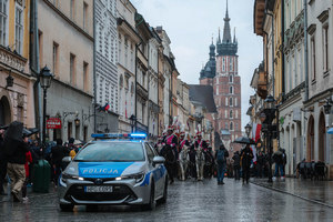 Radiowóz jadący przed pochodem trzeciomajowym na ul. Floriańskiej. W tle wieże kościoła mariackiego