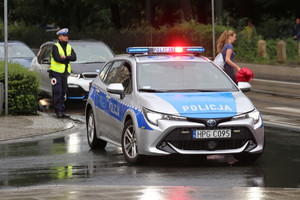 policjant ruchu drogowego i jego radiowóz na sygnałach blokuje przejazd ul. basztową