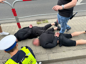 dwóch mężczyzn zatrzymanych po pościgu leżących na chodniku z kajdankami założonymi na ręce trzymane z tyłu