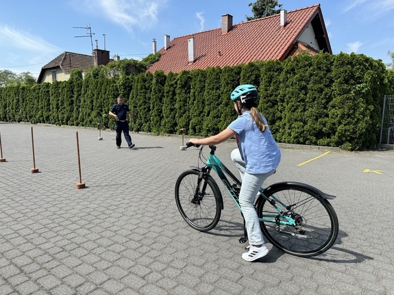 policjant nadzoruje część teoretyczną podczas egzaminu na kartę rowerową. uczennica przygotowuje się do pokonania toru przeszkód