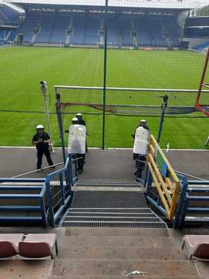 umundurowani policjanci wyposażeni w tarcze ochronne stoją przed schodami kierującymi na jedną z trybun stadionu