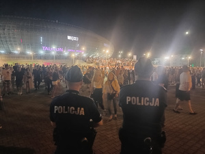 dwóch umundurowanych policjantów stojących przed Tauron Areną. W oddali widać tłum ludzi