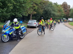 umundurowany policjant na motocyklu za którym znajduje się grupa uczniów jadących na rowerach