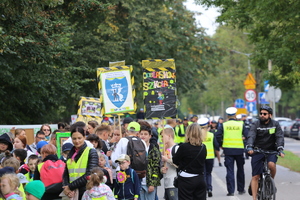 dzieci biorące udział w akcji trzymające transparenty promujące bezpieczeństwo. W oddali widać policjantów w kamizelkach odblaskowych