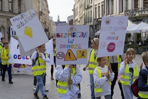 dzieci w kamizelkach odblaskowych uczestniczące w akcji z transparentami promującymi bezpieczeństwo na drodze