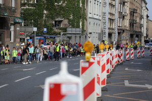 dzieci w kamizelkach odblaskowych w towarzystwie opiekunów idące przez jedną z głównych ulic Krakowa