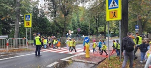 Przemarsz dzieci przez przejście dla pieszych, na pierwszym planie policjant kierujący ruchem