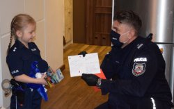 Komendant Miejski pokazuje dziewczynce podpisy policjantów znajdujące się wewnątrz kartki