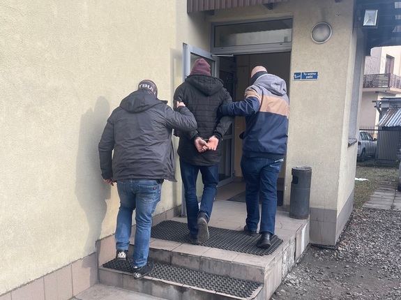 nieumundurowani policjanci wprowadzają do budynku komisariatu policji zatrzymanego mężczyznę