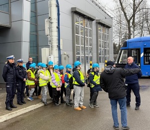 policjanci wraz z inspektorami MPK  oprowadzający grupe dzieci po zajezdni traamwajowej