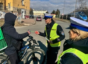 policjantka wręcza jadącemu rowerem element odblaskowy