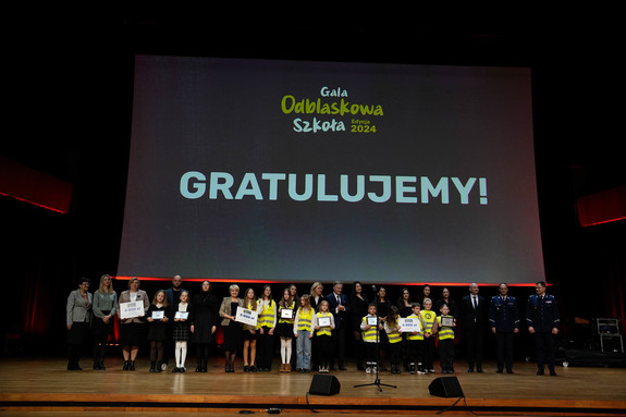 Na tle wyświetlonego baneru gratulujemy stoją uczniowie, nauczyciele z nagrodami wraz z policjantami