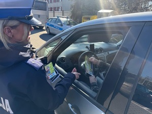 policjantka przekazuje kierowcy ulotki informacyjne i odblaski