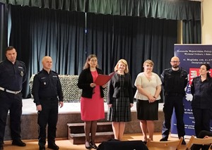 policjanci oraz nauczyciele jednej ze szkół stojący przed sceną w trakcie odczytywania laureatów konkursu