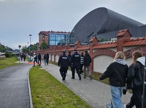 dwóch umundurowanych policjantów idących chodnikiem wśród studentów zmierzających na juwenalia