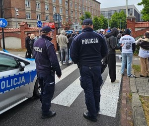 dwóch umundurowanych policjantów przy radiowozie obserwuje miejsce w którym świętują studenci