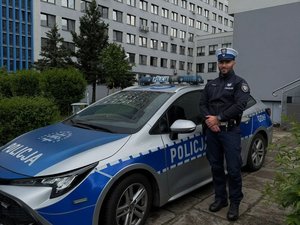 Policjant stoi obok radiowozu na tle komendy
