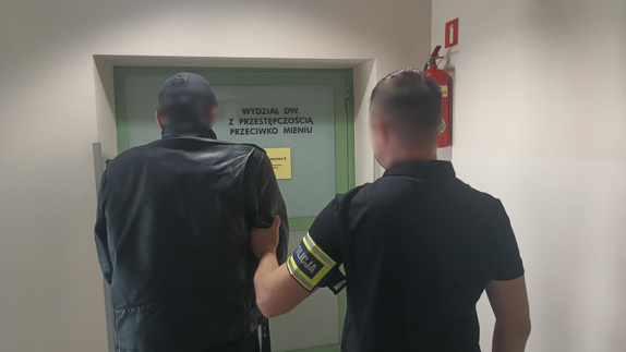nieumundurowany policjant prowadzi zatrzymanego mężczyznę do Wydziału zwalczającego przestępczość przeciwko mieniu krakowskiej komendy miejskiej