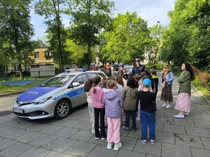 policjanci przy radiowozie omawiają z dziećmi zasady bezpieczeństwa na drodze