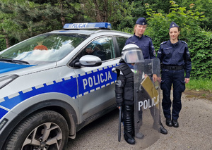 dziecko ubrane w elementy policyjnego umundurowania przy radiowozie pozuje do zdjęcia z policjantkami