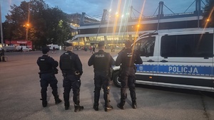 czterech umundurowanych policjantów stojących przy oznakowanym radiowozie zaparkowanym przy stadionie na ul. Reymonta
