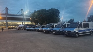czterech umundurowanych policjantów stojących przy oznakowanym radiwozie zaparkowanym przy stadionie na ul. Reymonta