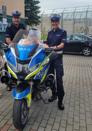 policjant, policjantka i dziecko w policyjnej czapce na słuzboym motocyklu