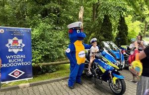 w krakowskim zoo dziecko siedząc na motocyklu pozuje do zdjęcia obok maskotka krakowskiej policji