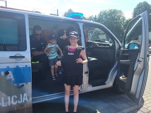 przy radiowozie dziewczynka z założoną kamizelką kuloodporną wewnątrz radiowozu policjant z dzieckiem