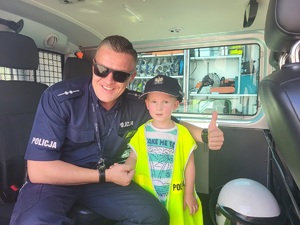 w radiowozie policjant i dziecko w policyjnej kamizelce odblaskowej