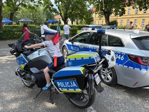 chłopiec siedzący na policyjnym motocyklu, obok radiowóz
