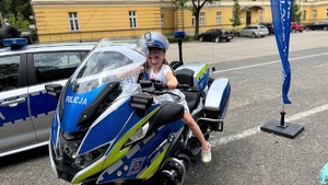 dziecko siedzące na policyjnym motocyklu w tle radiowóz i budynek