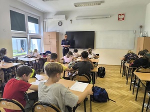 uczniowie w obecności policjantki piszą test wiedzy z zasad ruchu drogowego