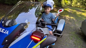 dziecko w policyjnej czapce z tarczą do zatrzymywania pojazdów siedzi na policyjnym motocyklu