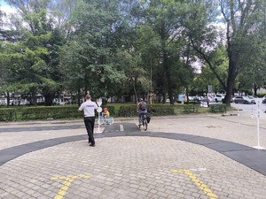 dziecko pokonujące na rowerze miasteczko rowerowe w towarzystwie policjanta i opiekuna