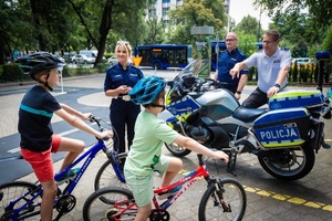 funkcjonariusze drogówki przy policyjnym motocyklu oraz dwoje dzieci na rowerach