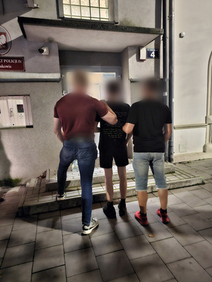 Policjanci operacyjni z zatrzymanym stoja przed komisariatem