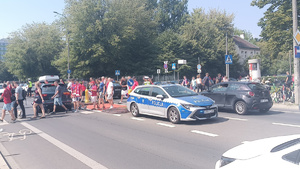 policjant stojący za radiowozem kieruje ruchem w rejonie przejścia dla pieszych przez które przechodzą osoby udające się na mecz