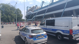policyjne radiowozy stojące przy stadionie. W oddali widać kibiców udających się na stadion