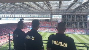 policyjne radiwozoy stojące przy stadionie. W oddali widać kibiców udających się na stadion