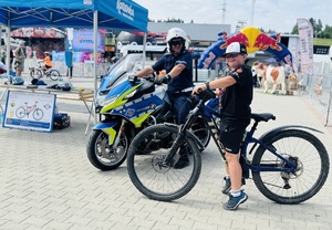 policjant na motocyklu obok których stoi chłopiec na rowerze