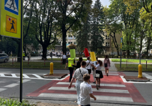 grupa uczniów przechodzi na drugą stronę jezdni w asyście policjantki