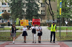 policjantka asystuje dzieciom biorącym udział w akcji w przechodzeniu przez jezdnię