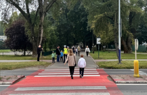 policjantki na chodniku rozmawiają z grupą osób, a dwie osoby przechodzą przez przejście dla pieszych