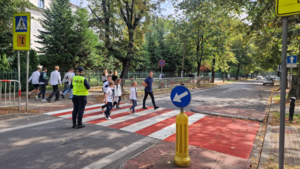 osoby przechodzące przez przejście dla pieszych i policjantka dbająca o ich bezpieczeństwo